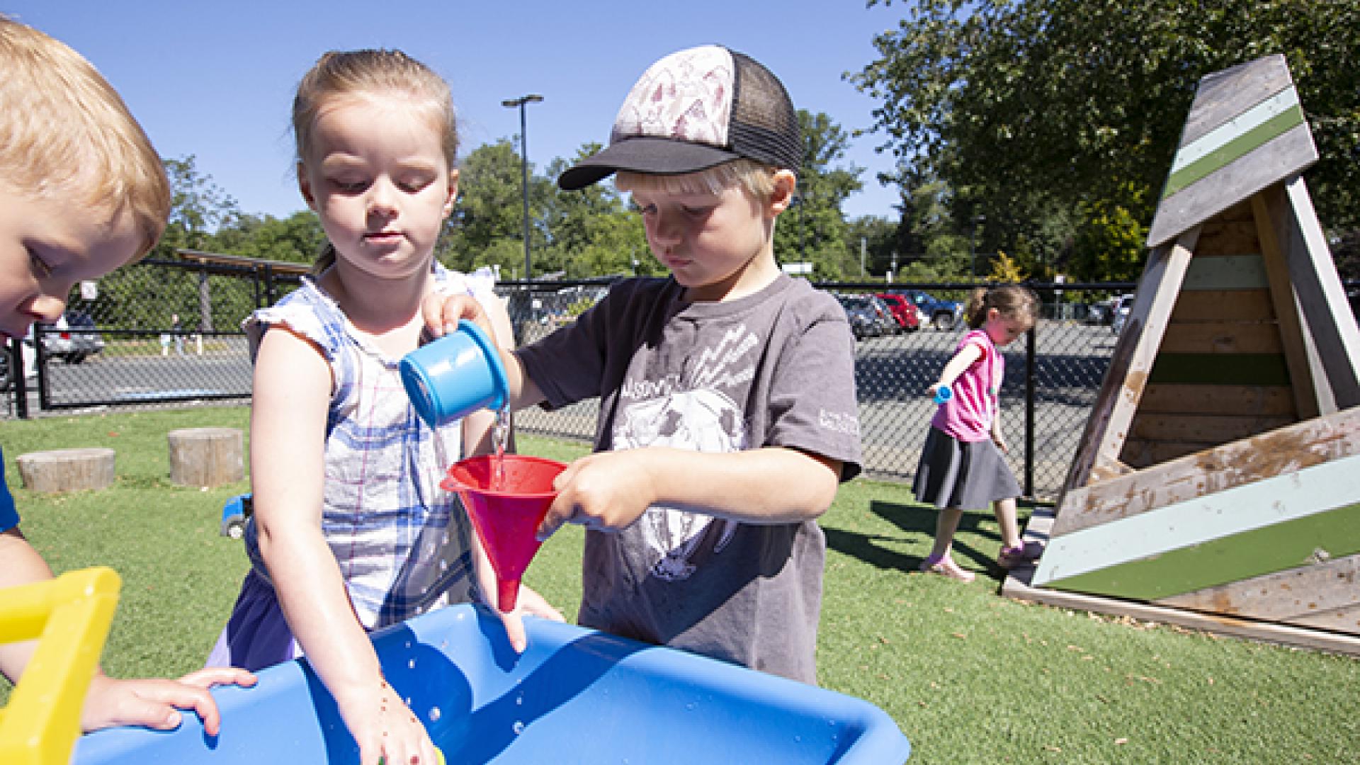A girl and a boy playing at an outdoor sand table