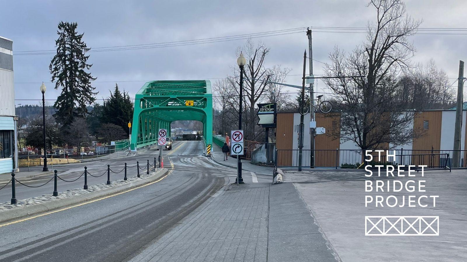 Teal bridge at the endo of a road. There are some buildings in the foreground.