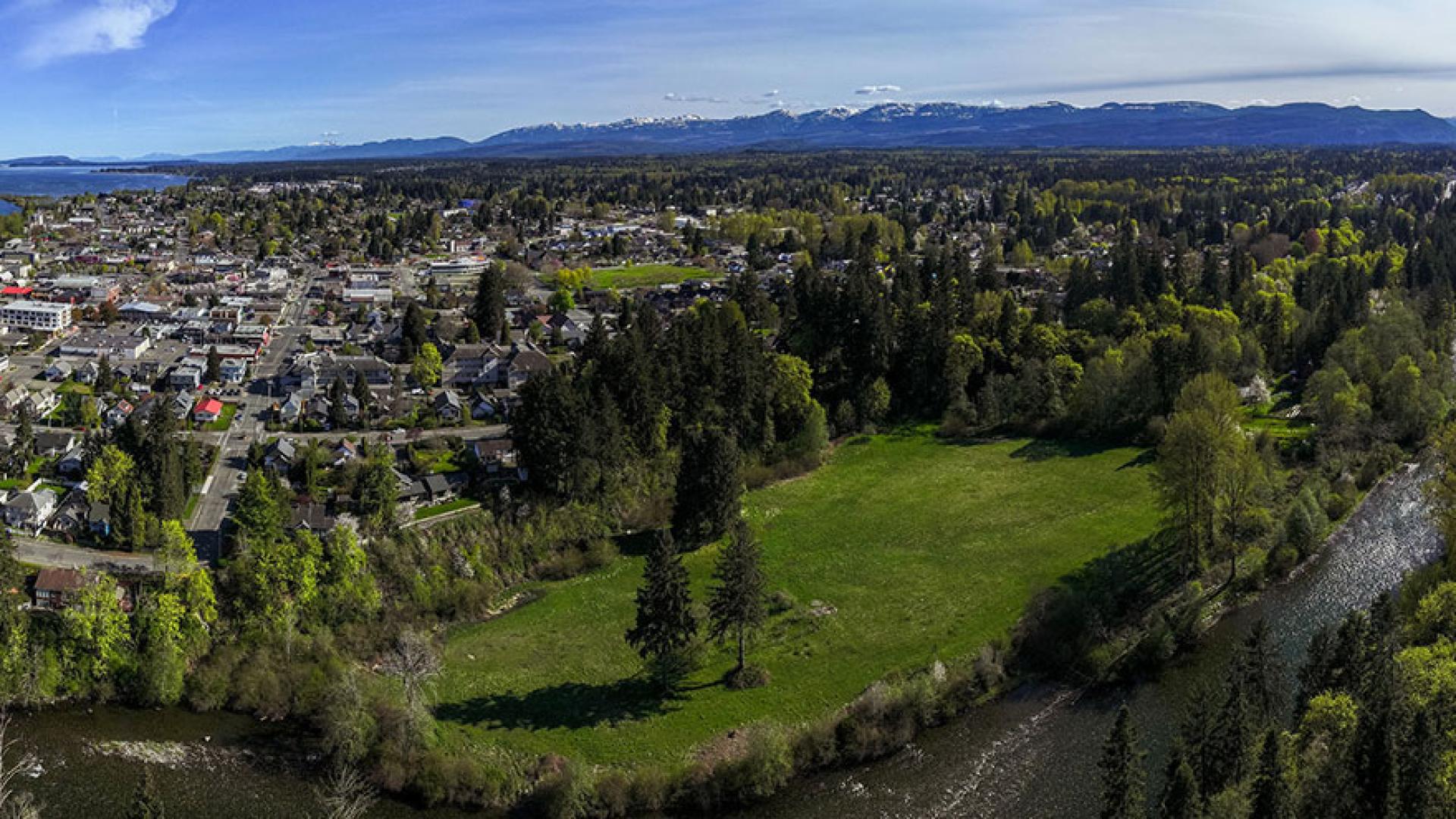 Aerial view of McPhee Meadows and the Puntledge River, looking south toward City of Courtenay, mountains and blue sky.
