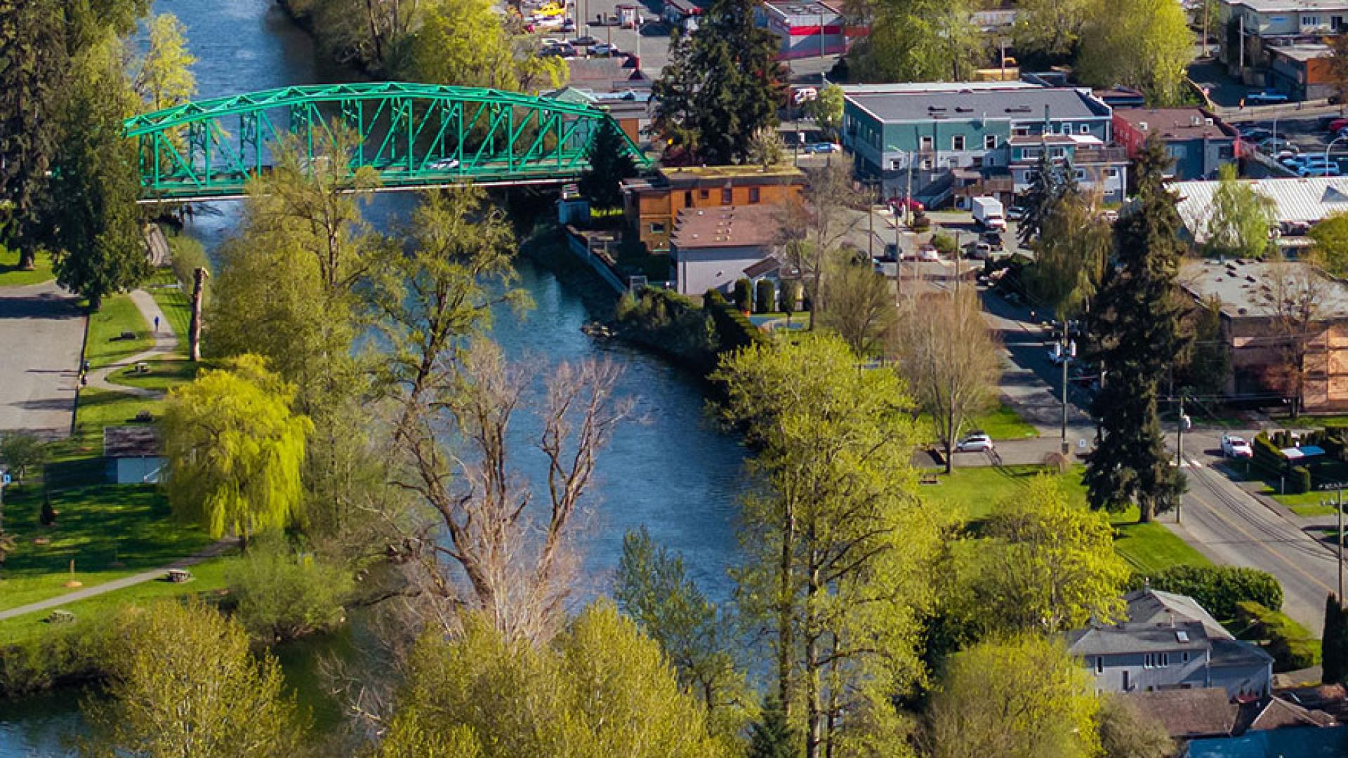 An aerial image of the Courtenay River looking south toward the 5th Street Bridge, overlooking the Anderton Avenue retaining wall. Part of Downtown Courtenay is in the background..